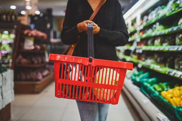 Mujer caminando en una tienda de comestibles sosteniendo una cesta de compras roja