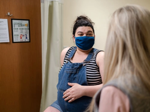 ကျန်းမာရေးစစ်ဆေးနေစဉ်အတွင်း ဆရာဝန်၏ရုံးခန်းတွင် မျက်နှာဖုံးတပ်ထားသော ကိုယ်ဝန်ဆောင်အမျိုးသမီး